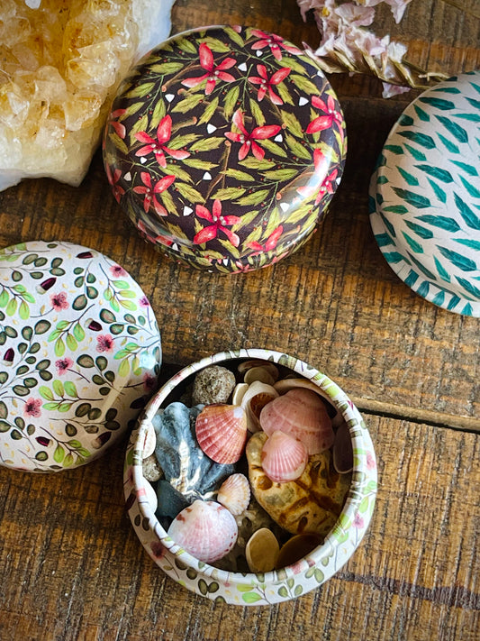 This image features a collection of beautifully designed mini mystery tins, each adorned with vibrant, ocean-inspired patterns. These tins, known as the Sea Witch Mini Mystery Tins, are filled with an assortment of tiny seashells and natural wonders, carefully curated to appeal to those interested in magickal and craft purposes.