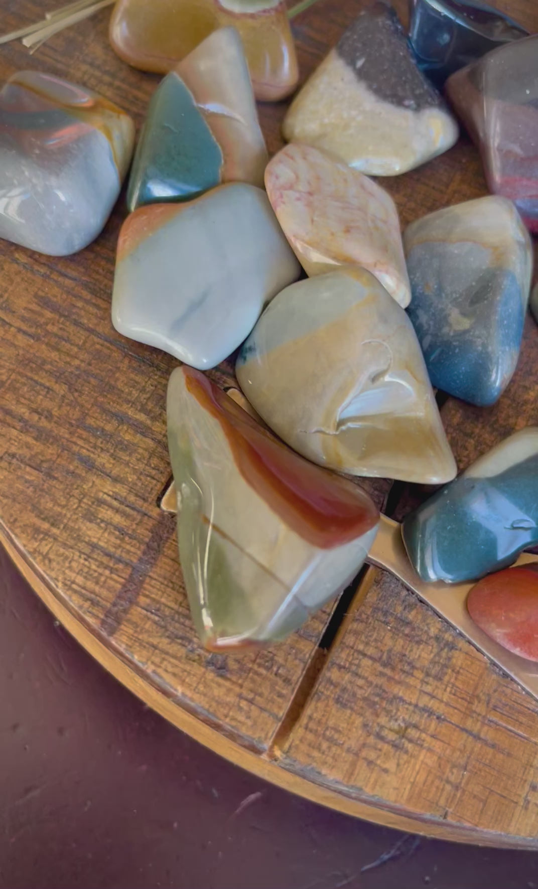 Up close look at Tumbled polychrome jasper (desert jasper) laid out on a wooden surface.