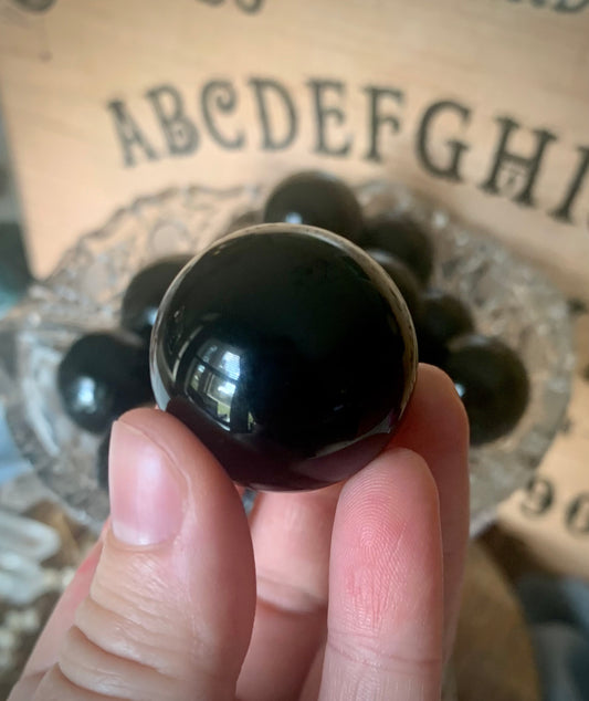 A sphere of black obsidian held up close with many more in the background in a crystal dish.