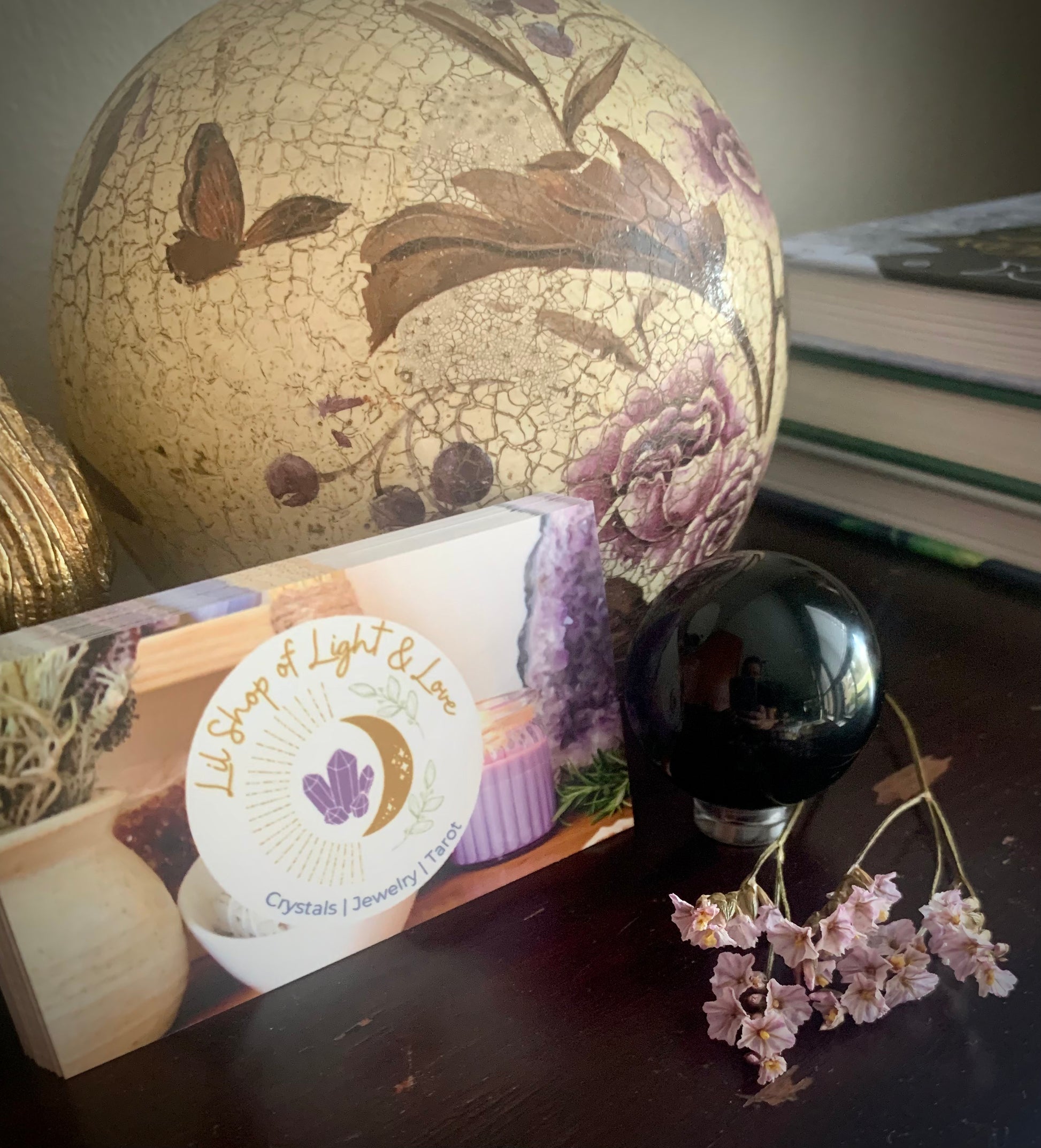 Black obsidian sphere displayed on a dark wooden desk next to business cards for lil shop and dried pink flowers 