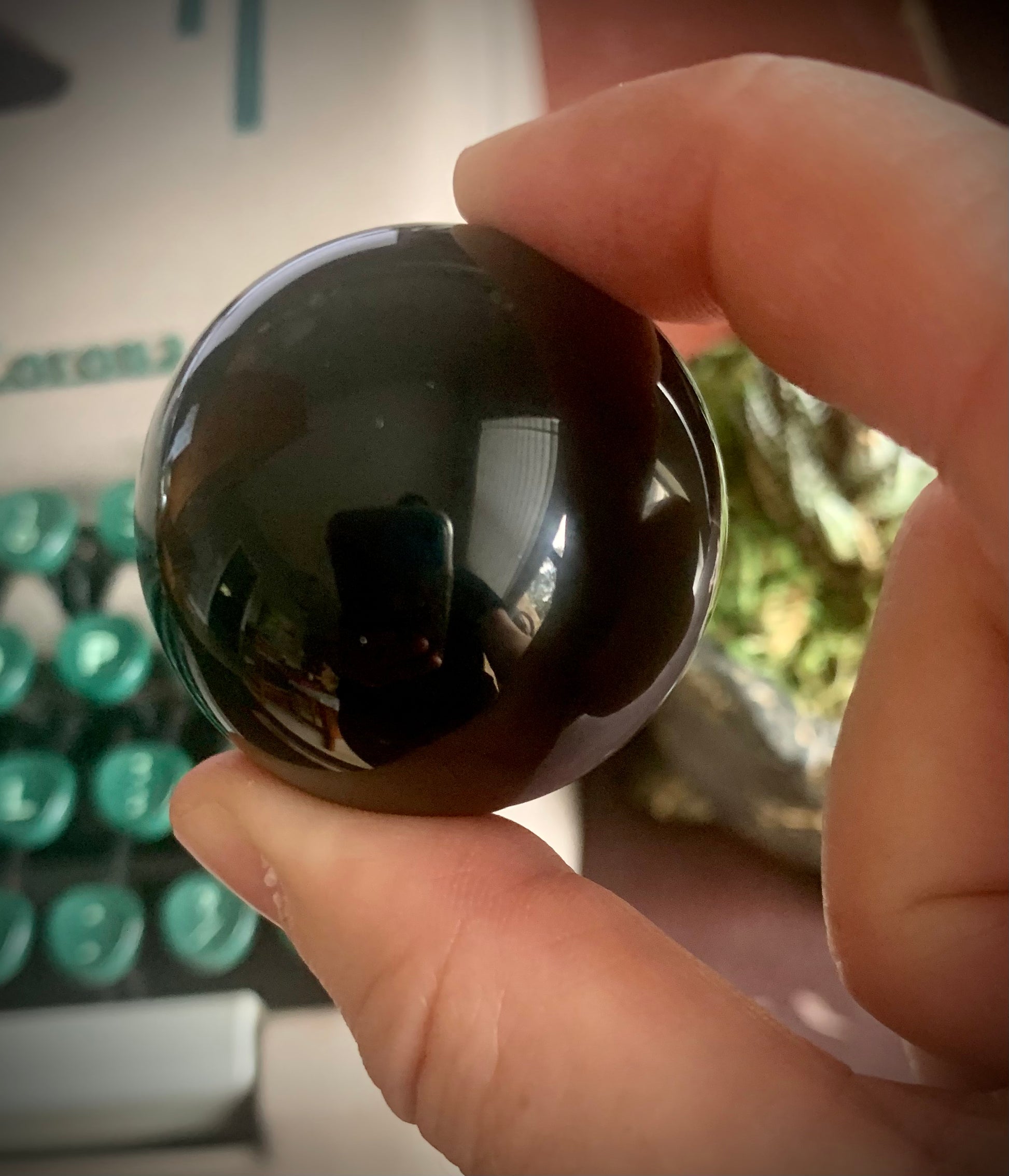 Black obsidian sphere held in between two fingers in front of a green typewriter.